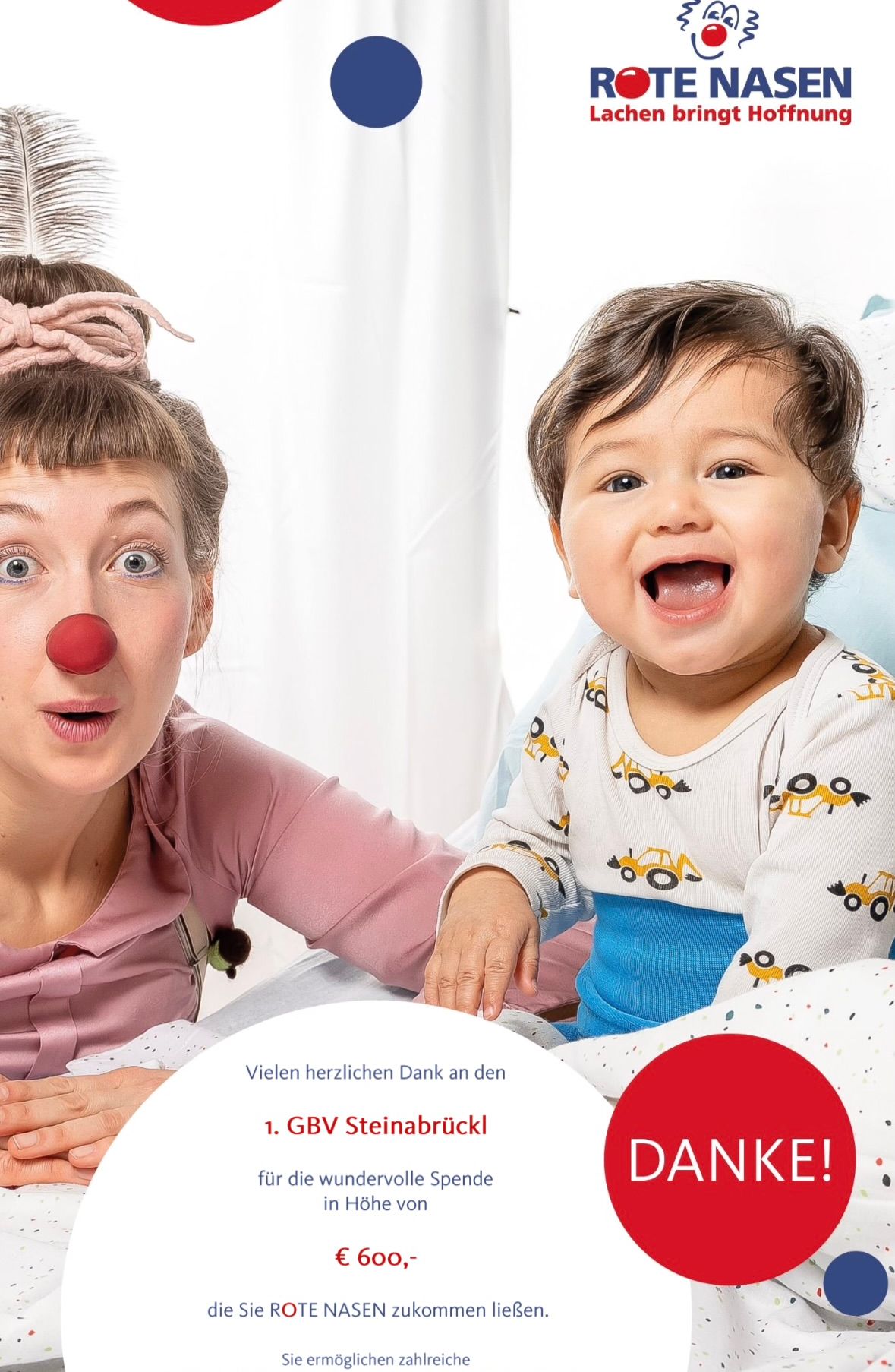 A woman wearing a pink shirt and a red clown nose is playing with a baby in a high chair. The baby is wearing a blue and white onesie with yellow construction vehicles on it.