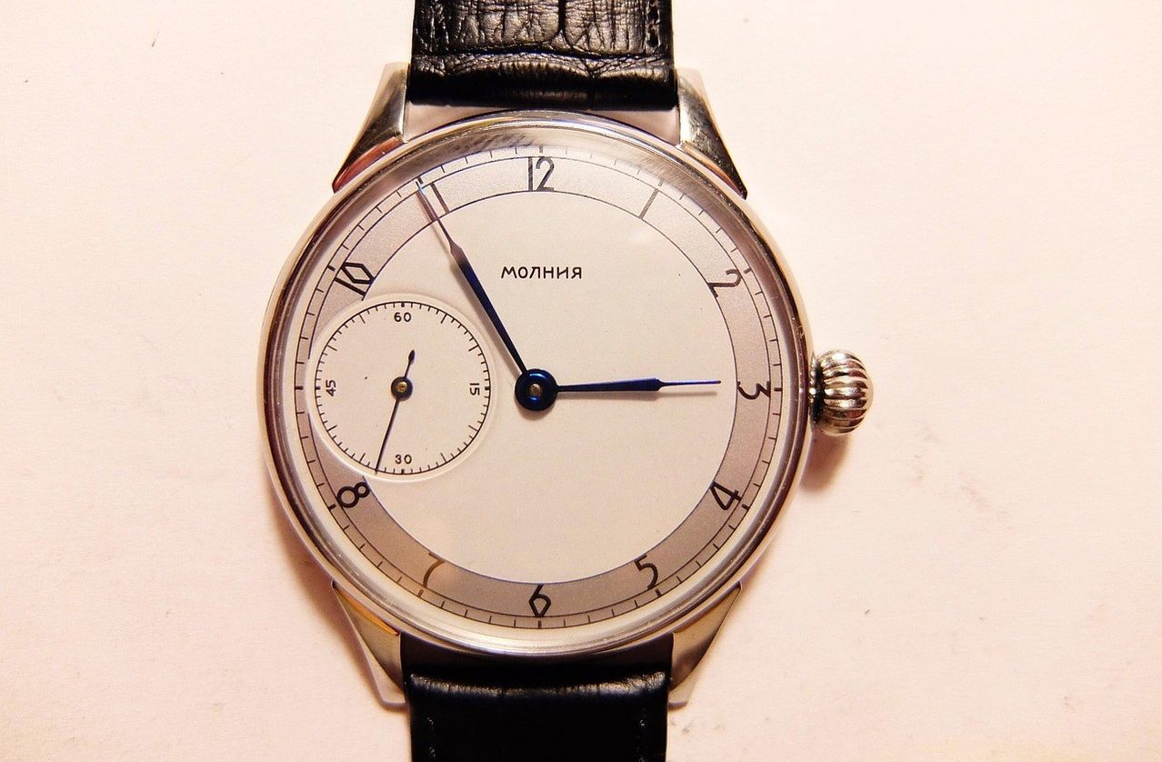 Eine silberne Armbanduhr mit schwarzem Lederarmband zeigt die Zeit als 10:10 an. Sie hat eine kleine Ziffer für Sekunden und eine weitere für Minuten. Das Zifferblatt der Uhr hat römische Zahlen.