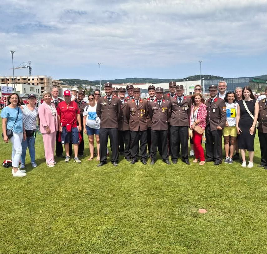 Eine Gruppe von Menschen in Uniform und Freizeitkleidung steht auf einem grünen Feld, möglicherweise für ein Gruppenfoto.