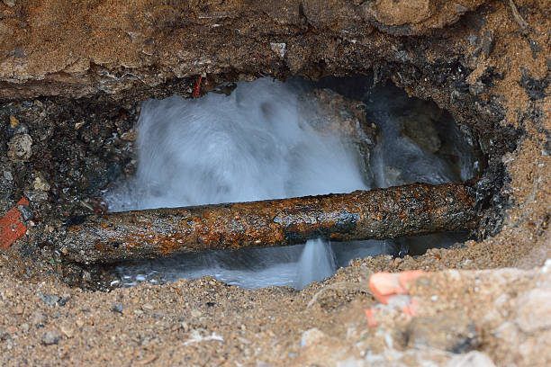 A rusty pipe is leaking water into a hole in the ground. The water is flowing out of the pipe and into the hole.