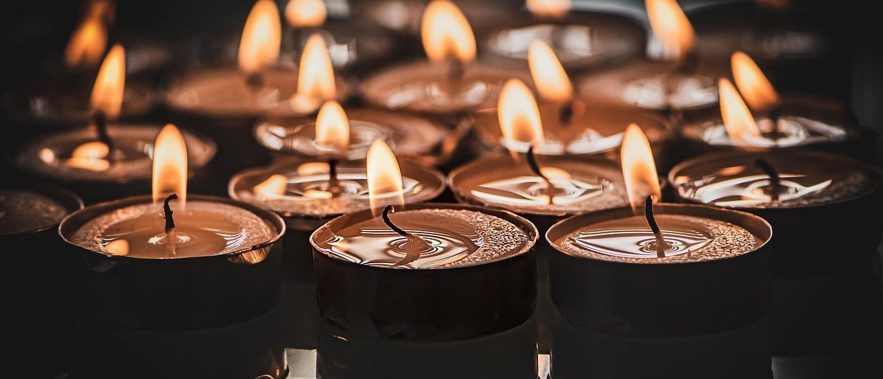 Eine Nahaufnahme von mehreren brennenden Kerzen in verschiedenen Brennphasen, die ihre Umgebung mit ihrem warmen Licht erhellen.