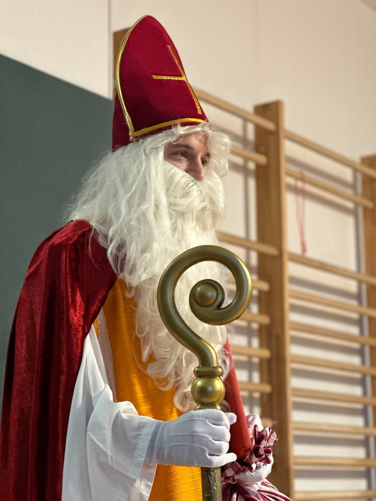 Eine Person, die als St. Nikolaus verkleidet ist, hält einen goldenen Stab in der Hand und trägt einen roten Hut und einen langen weißen Bart.