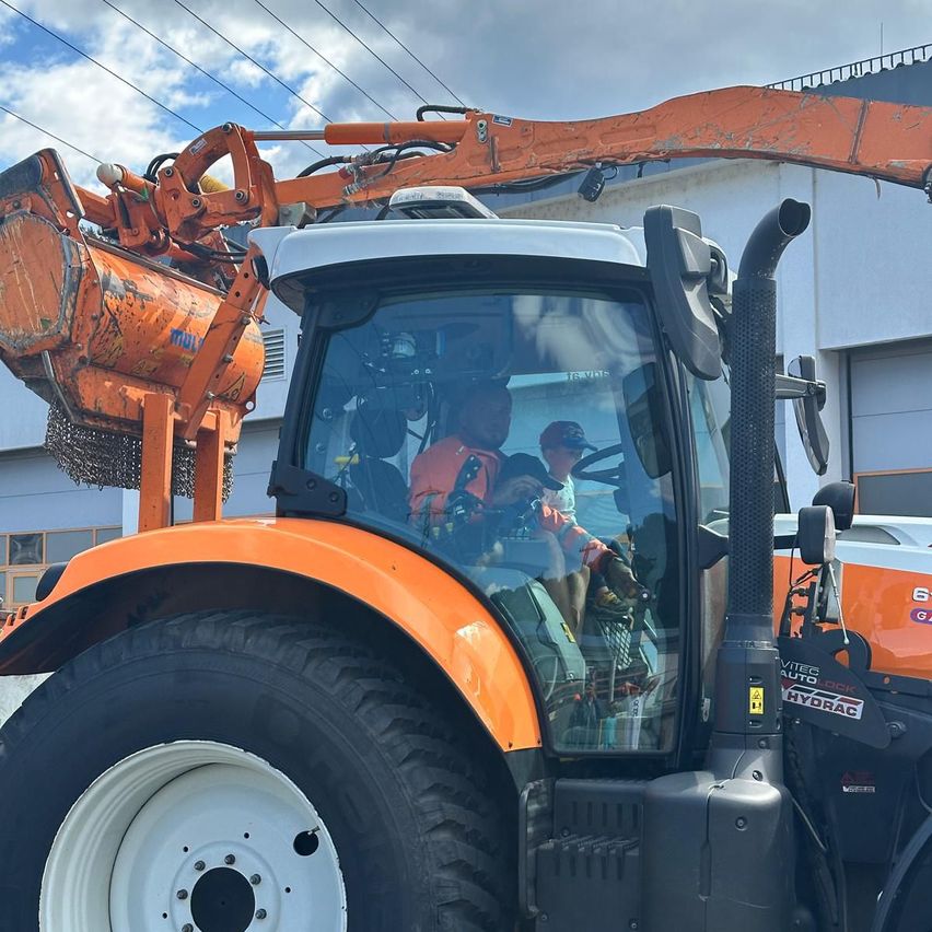 Ein großer orangefarbener Traktor mit einer Person im Inneren und einer weiteren Person außerhalb. Der Traktor hat eine große orangefarbene Vorrichtung vorne.