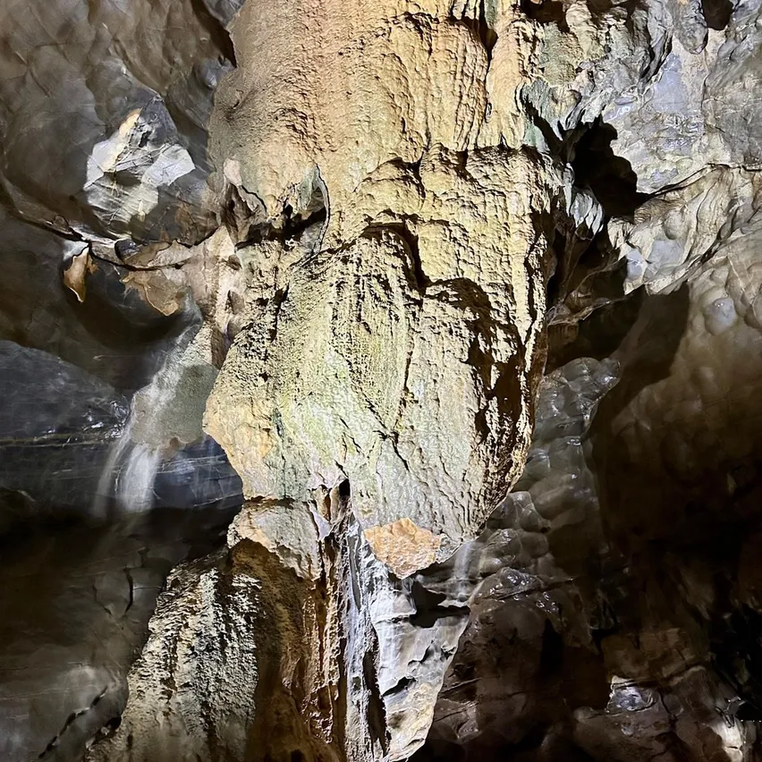 Eine große, strukturierte Felsformation in einer Höhle mit einem Wasserfall, der von oben tropft.