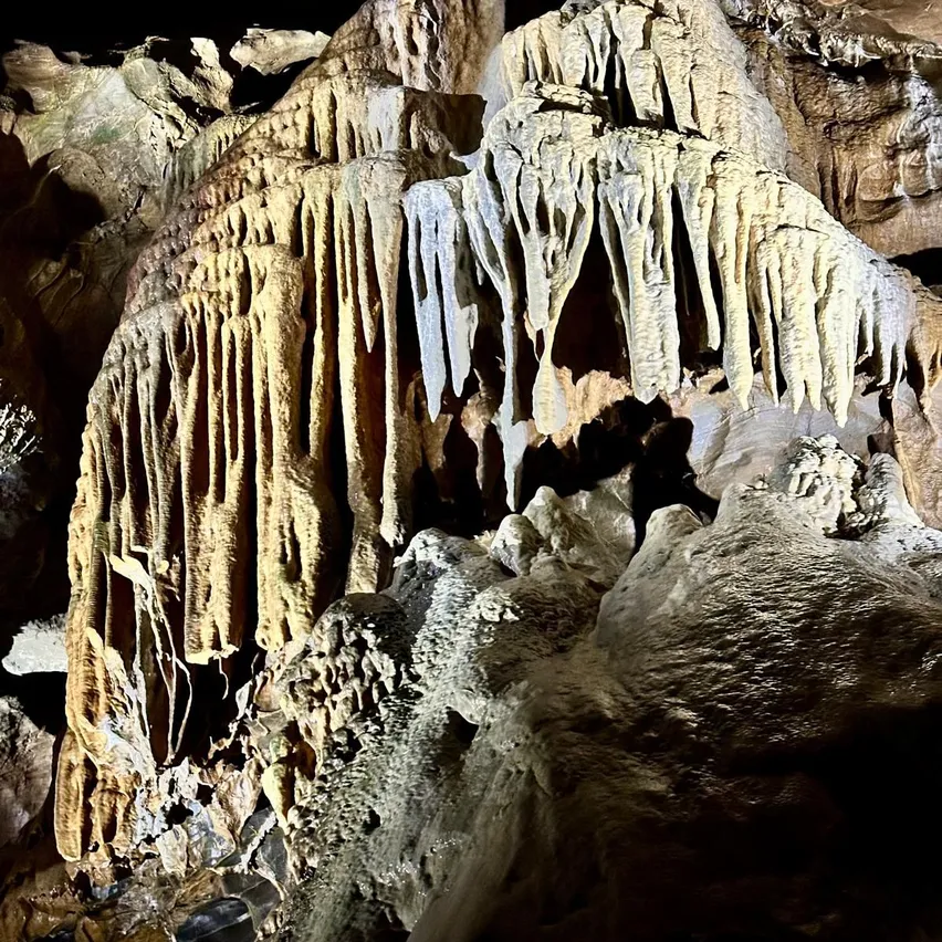 Eine Höhle mit großen Stalaktiten und Stalagmiten, beleuchtet von einer Lichtquelle, die komplizierte Formationen und Felsstrukturen zeigt.