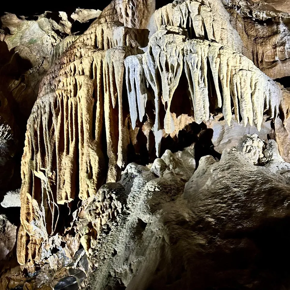 Eine Höhle mit großen Stalaktiten und Stalagmiten, beleuchtet von einer Lichtquelle, die komplizierte Formationen und Felsstrukturen zeigt.