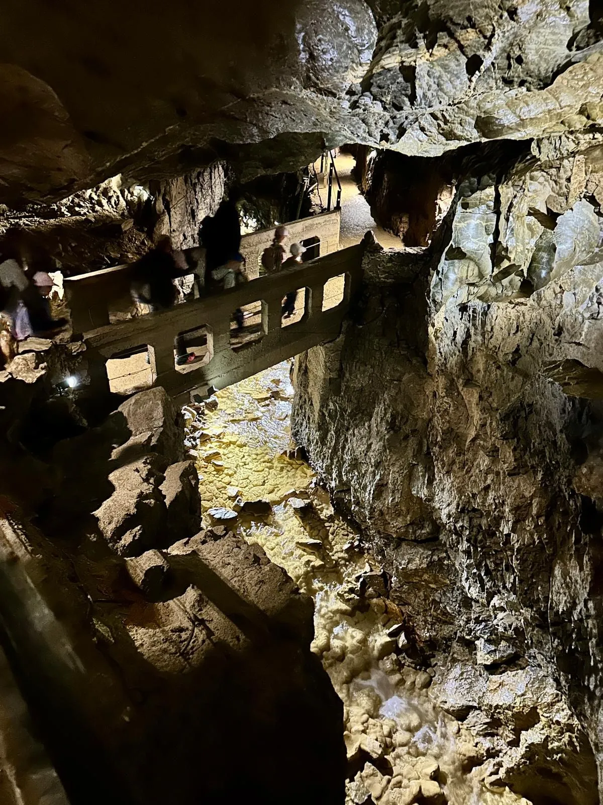 Eine Gruppe von Menschen geht auf einer hölzernen Brücke in einer Höhle mit einem schmalen Bach darunter.