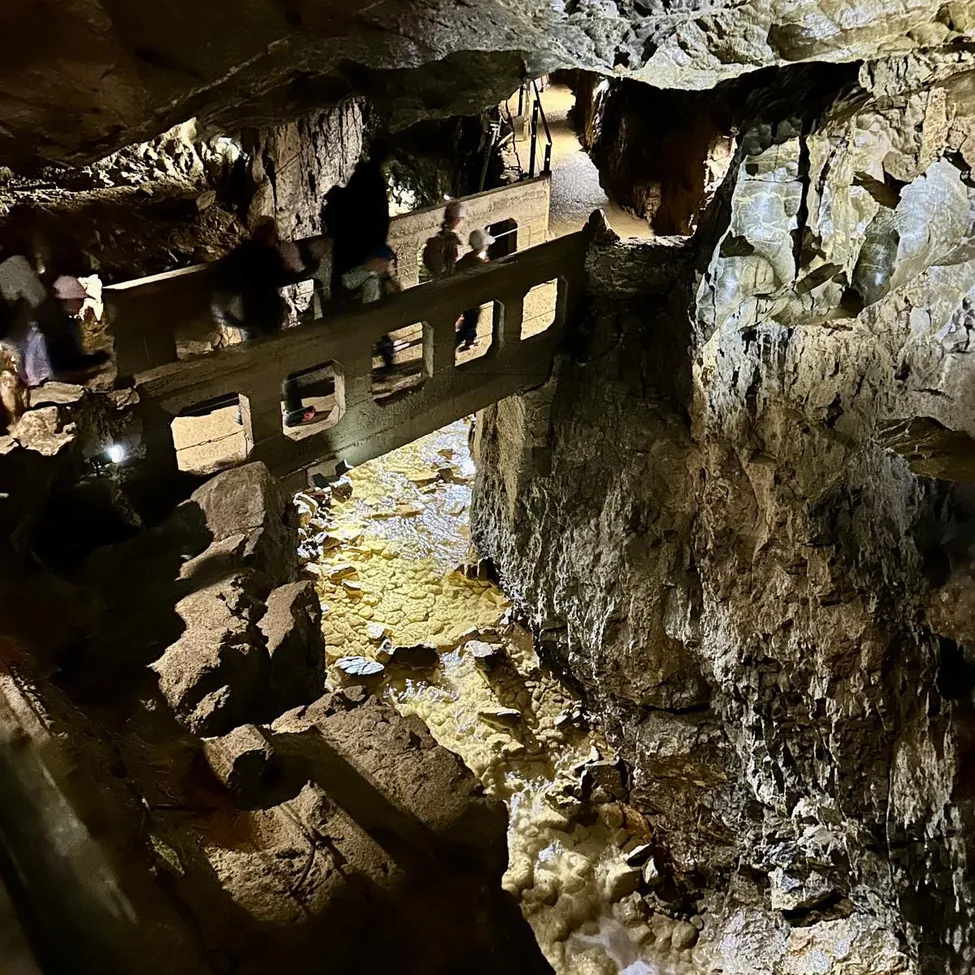Eine Gruppe von Menschen geht auf einer hölzernen Brücke in einer Höhle mit einem schmalen Bach darunter.