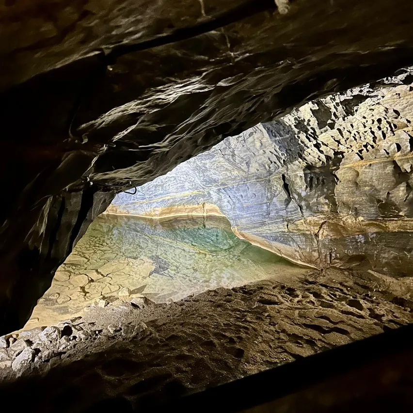 Ein Blick von innen in eine Höhle mit einem Wasserbecken, umgeben von felsigen Wänden. Das Wasser ist klar und reflektiert die Höhlendecke.