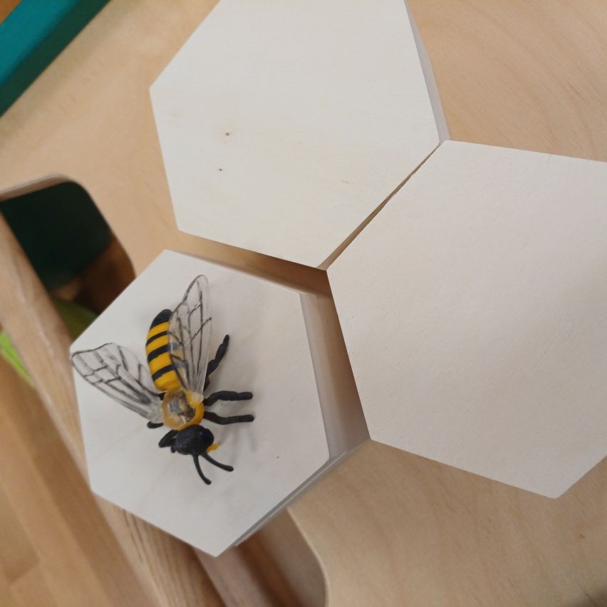 A white hexagonal toy on a wooden surface, featuring a bee figurine with black and yellow stripes and transparent wings.
