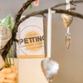 Ein Tisch mit einem Buch betitelt 'Petting' mit einem goldenen Kreis. Es enthält eine Vase mit Blumen, Kerzen und herzförmigen Ornamenten.