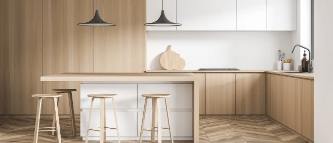 Moderne Küche mit Holzböden, Insel und zwei schwarzen Pendelleuchten. Schränke und Arbeitsplatten sind weiß. Hocker umgeben die Insel.