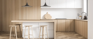 Moderne Küche mit Holzböden, Insel und zwei schwarzen Pendelleuchten. Schränke und Arbeitsplatten sind weiß. Hocker umgeben die Insel.