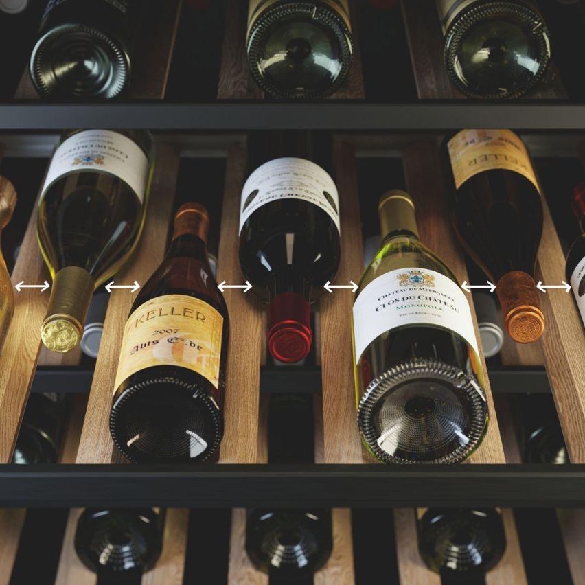 Ein hölzerne Weinregal zeigt mehrere Weinflaschen, darunter eine Keller 2007 Flasche, mit Pfeilen nach rechts, was auf eine Reihenfolge oder Richtung hinweist.