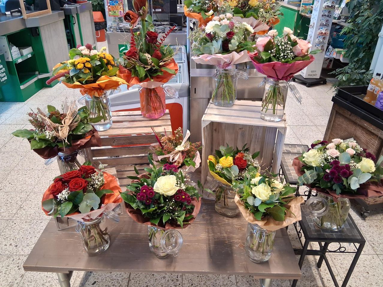 Multiple vases of flowers arranged on a wooden table, each vase filled with various flowers in different colors, and some vases covered with paper.