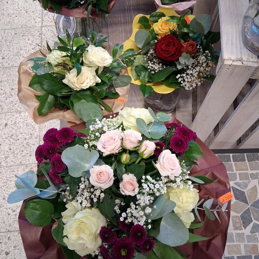 A bouquet of white and pink roses and baby's breath is on a table, next to a smaller bouquet of red and yellow roses in a yellow vase.