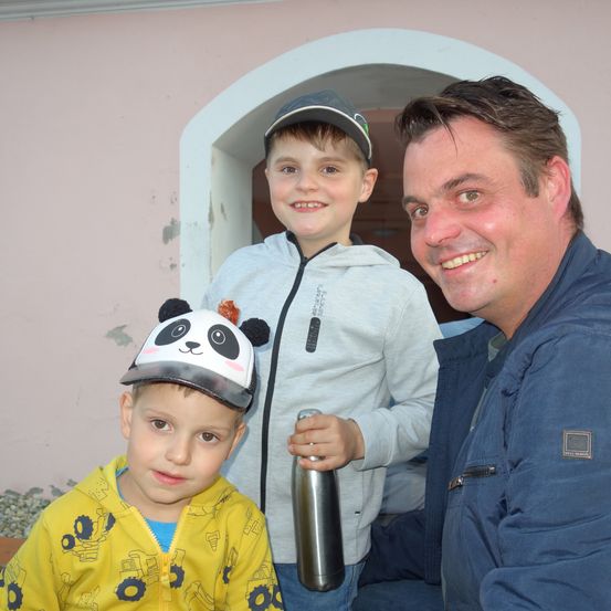 Zwei Jungen und ein Mann lächeln für die Kamera, ein Junge trägt einen Panda-Hut, der andere einen Cap, und der Mann hält eine Edelstahlflasche.