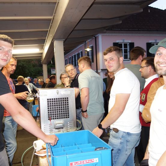 Eine Gruppe von Männern steht und plaudert in einer Schlange, einer der Männer zapft ein Bier.