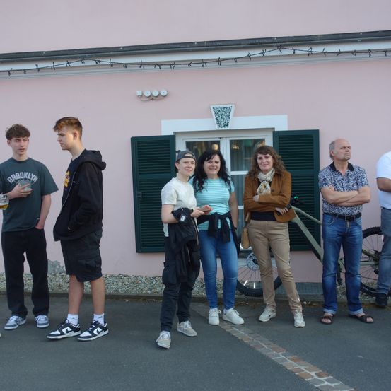 Eine Gruppe von Menschen steht vor einem rosa Gebäude, hinter dem ein Fahrrad geparkt ist.