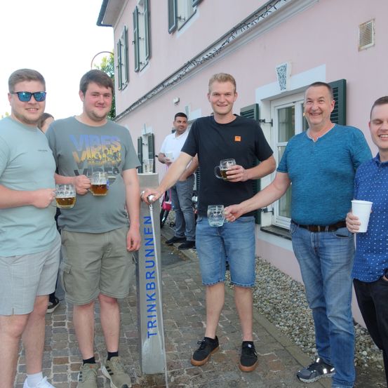 Fünf Männer stehen vor einem Gebäude. Sie alle lächeln und halten Gläser mit Bier in der Hand.