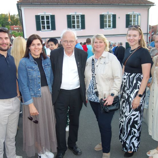 Eine Gruppe von Menschen, darunter zwei Frauen und zwei Männer, steht vor einem rosa Gebäude.