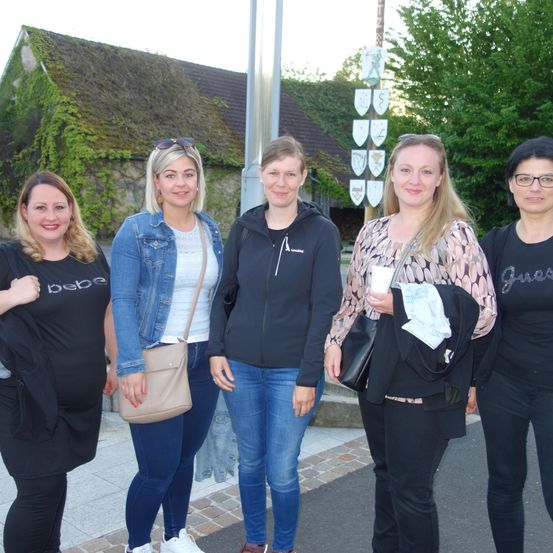 Fünf Frauen stehen nebeneinander vor einem mit Efeu bewachsenen Gebäude.