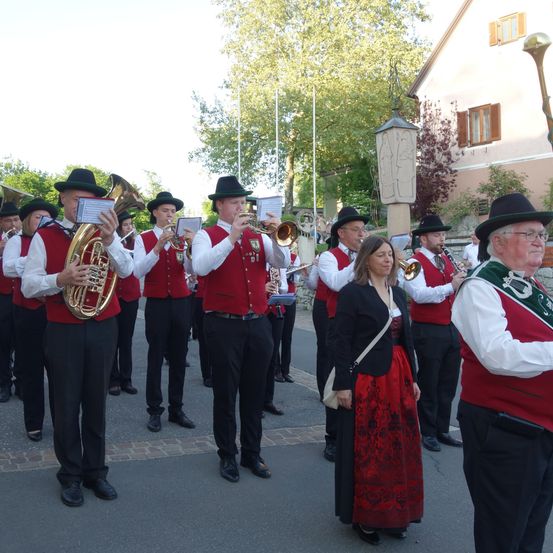 Eine Blaskapelle in roten Westen und schwarzen Hosen steht in einer Reihe und spielt ihre Instrumente vor einem Gebäude.