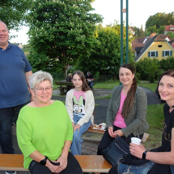 Eine Gruppe von Menschen sitzt auf einer Bank draußen, lächelt und posiert für ein Foto.