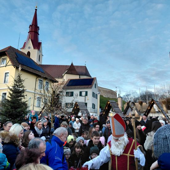 Eine Menschenmenge versammelt sich um eine Kirche mit Solarpanels, während ein Mann als Weihnachtsmann gekleidet den Weg leitet.