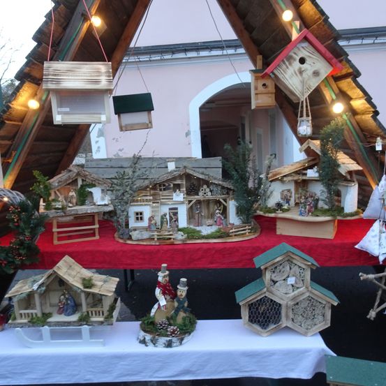 Eine Weihnachtsausstellung mit Holzhäusern und Krippenszenen auf einem Tisch, umgeben von hängenden Vogelhäusern und kleinen Dekorationen.