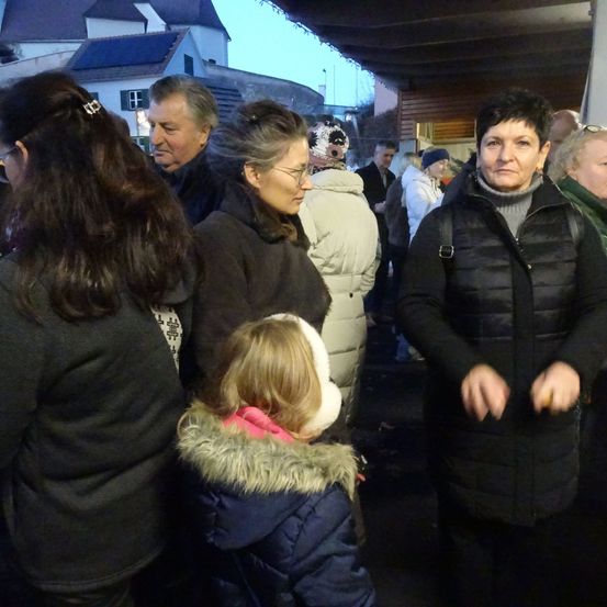 Eine Gruppe von Erwachsenen und Kindern hat sich unter einem Schutzdach versammelt und schaut in die gleiche Richtung. Das Wetter scheint kalt zu sein.