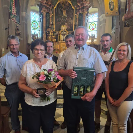 Eine Gruppe von Menschen, darunter ein Mann und eine Frau, posiert für ein Foto in einer Kirche, einer hält Blumen und eine Geschenkbox.