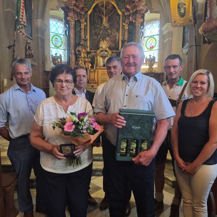 Eine Gruppe von Menschen, darunter ein Mann und eine Frau, posiert für ein Foto in einer Kirche, einer hält Blumen und eine Geschenkbox.