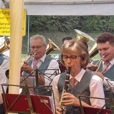 Eine Gruppe von Musikern, darunter eine Frau, die eine Klarinette spielt, tritt unter einem Zelt mit einem gelben Schild im Hintergrund auf.