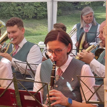 Eine Gruppe von Musikern spielt Instrumente, darunter ein Mann, der Klarinette spielt, in einer Außenumgebung.