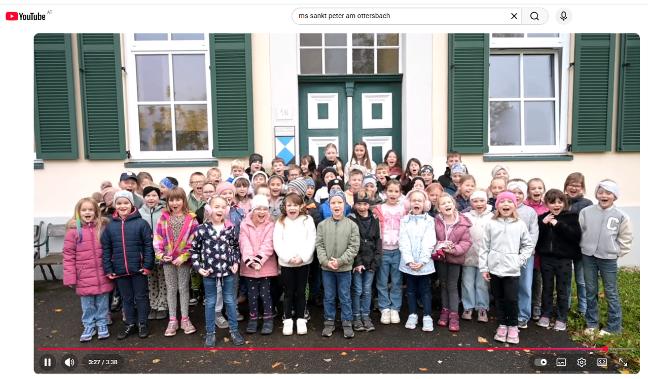Eine große Gruppe von Kindern, in Winterkleidung gekleidet, posiert für ein Foto vor einem Gebäude mit großen Fenstern und einer grünen Tür.