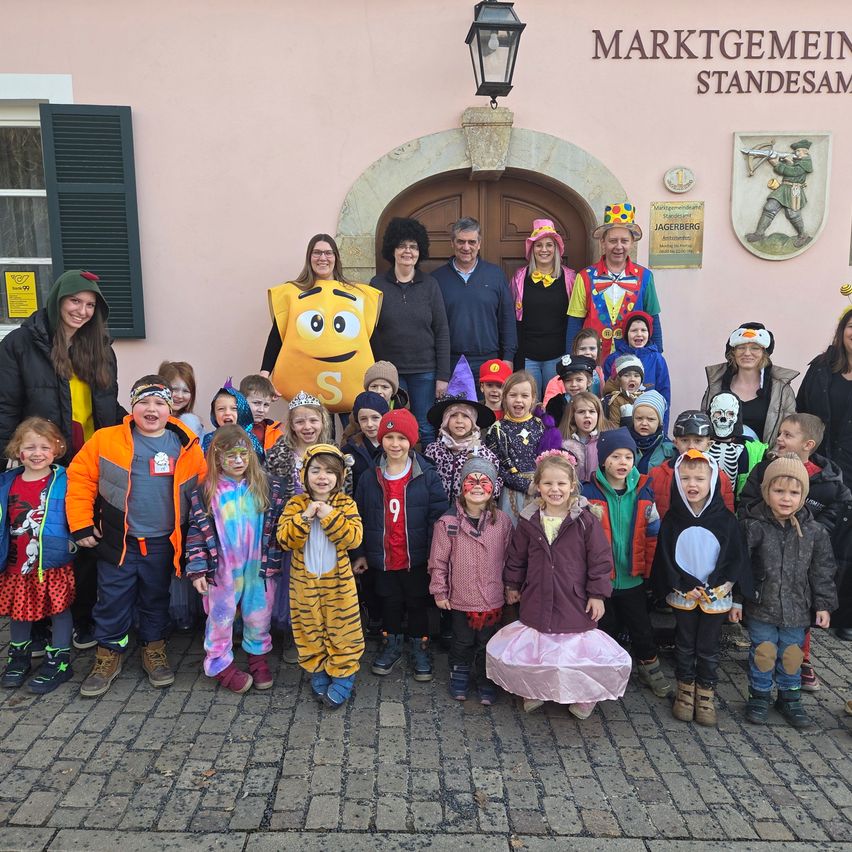 Eine Gruppe von Kindern und Erwachsenen in Kostümen posiert für ein Foto vor einem Gebäude mit der Aufschrift 'Marktgemeinde Standesam' über der Tür.