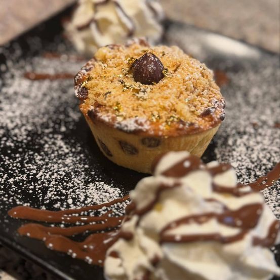 Ein Nahaufnahme einer Schokoladen-Chip-Keks-Tarte mit goldener Streuselkruste und Schokoladen-Drizzle, serviert auf einem schwarzen Teller.