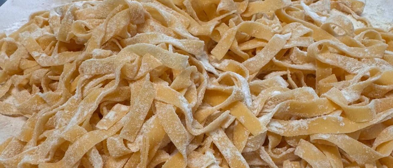 Nahaufnahme von frisch zubereiteter Fettuccine-Pasta, bestreut mit Mehl, auf einer mehlbestreuten Oberfläche.