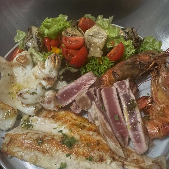 Ein Teller mit Meeresfrüchten und Salat mit Garnelen, Thunfisch und Artischocken auf einer Metalloberfläche.
