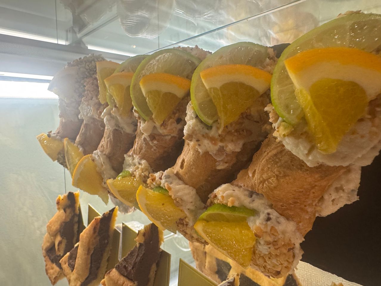 A close-up view of several pastries, each topped with a slice of lemon or lime, displayed in a glass case.