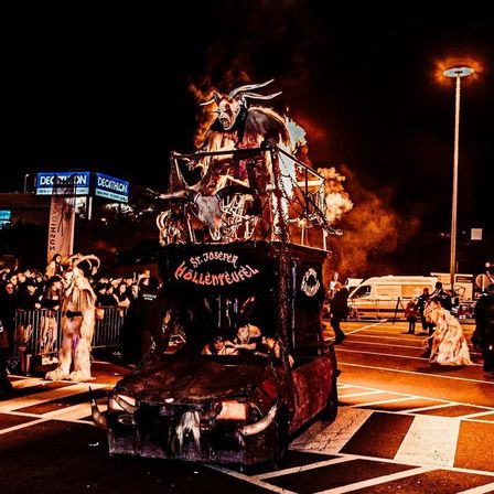 Ein Halloween-Umzug mit einem geschmückten Fahrzeug und einer Person mit Hörnern darauf, umgeben von einer Menge.