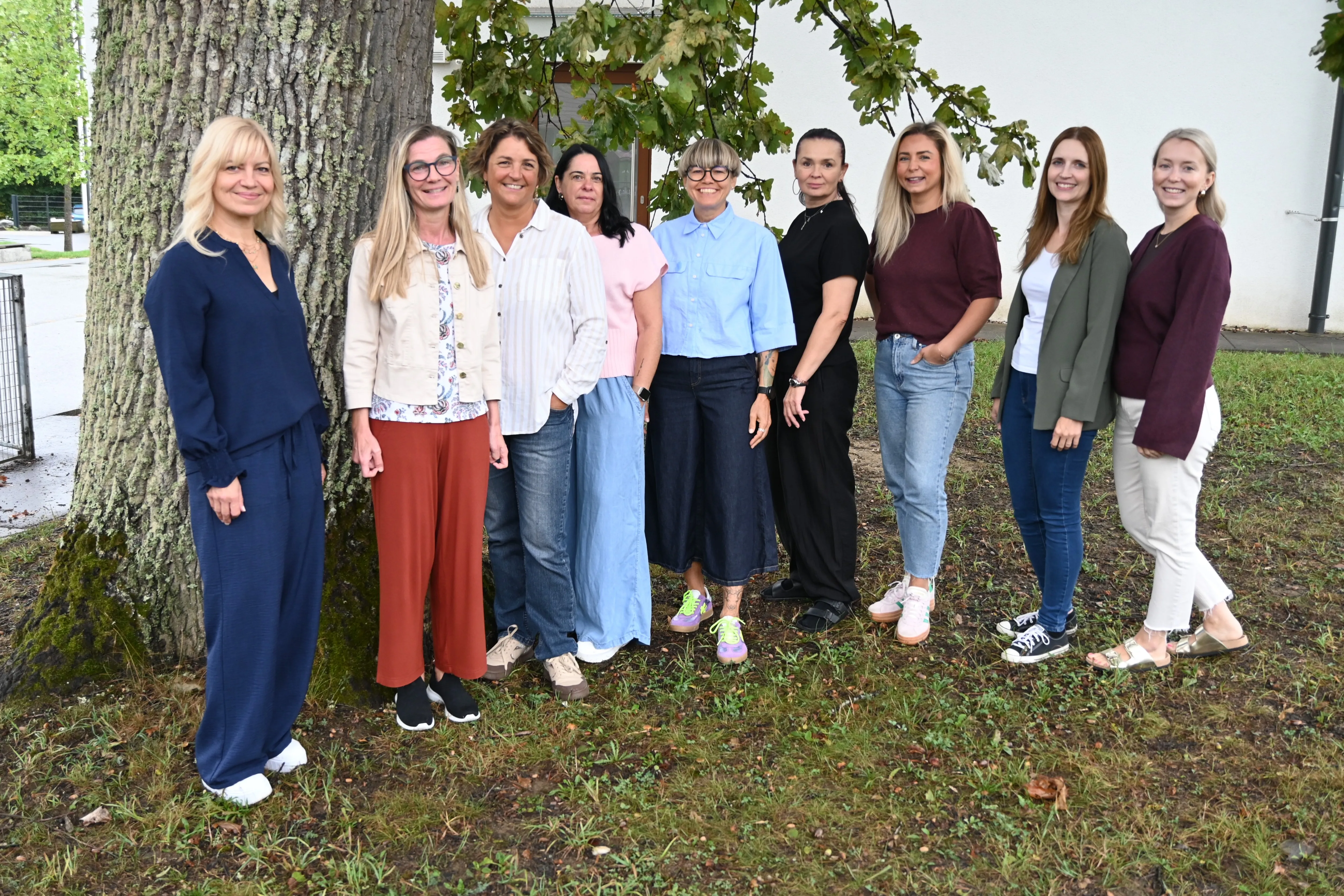 Eine Gruppe von Frauen in verschiedenen Outfits steht in einem Park und lächelt für ein Foto.