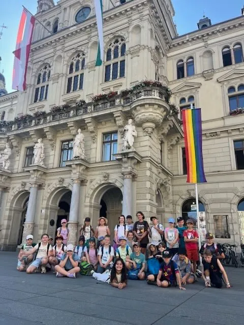 Eine Gruppe von Kindern posiert vor einem historischen Gebäude mit Fahnen und Statuen an der Fassade.
