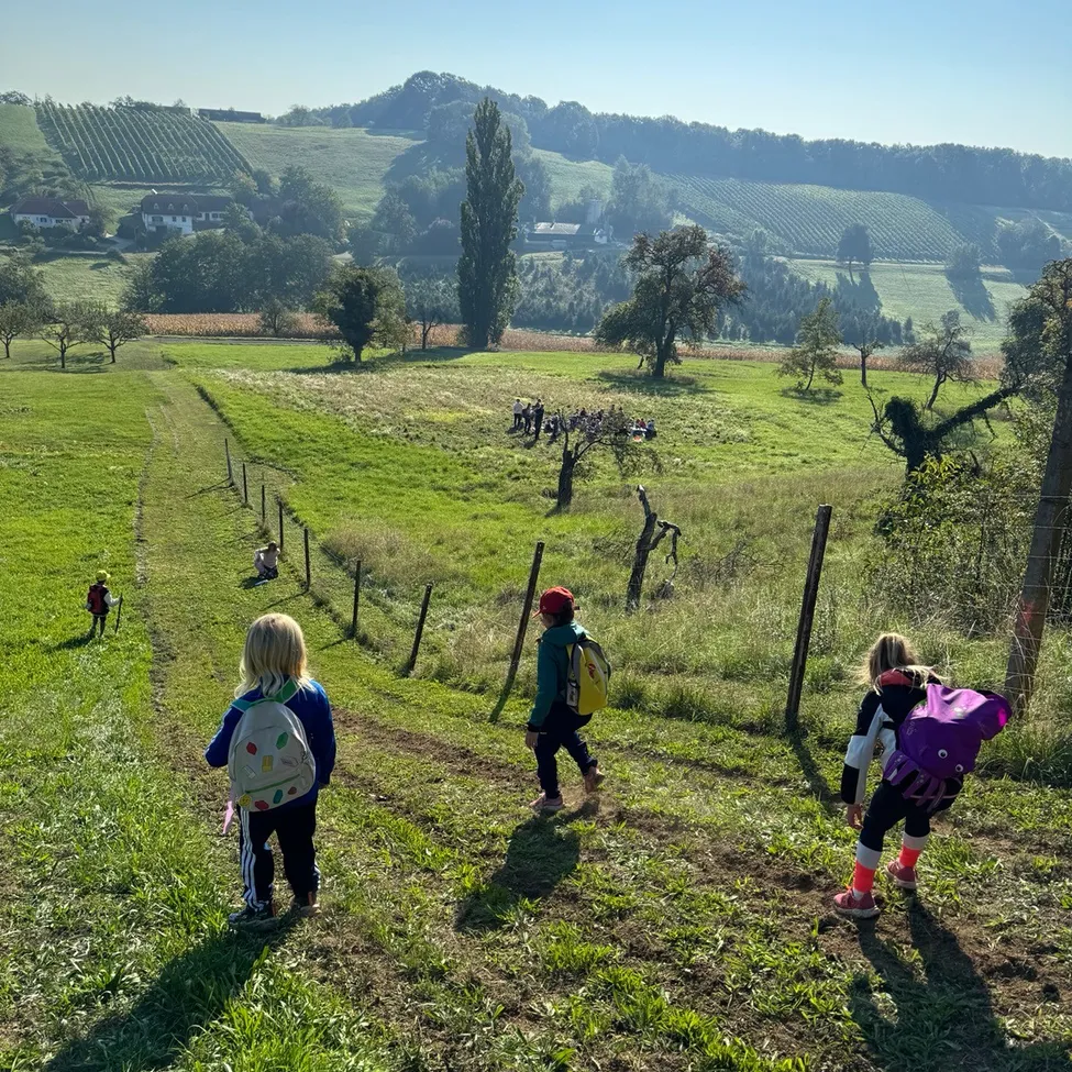 Eine Gruppe von Kindern geht auf einem Grasfeld und trägt Rucksäcke.