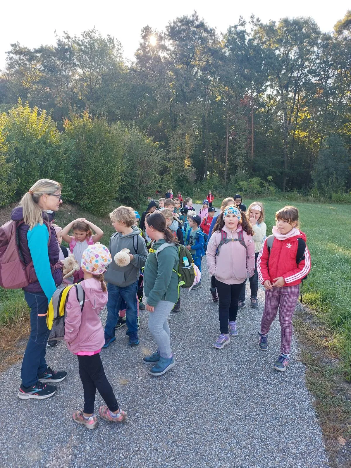 Eine Gruppe von Kindern, wahrscheinlich auf einer Schulfahrt, geht auf einem Kiesweg in einem Park. Sie werden von einer Frau begleitet, die wahrscheinlich ihre Lehrerin ist.
