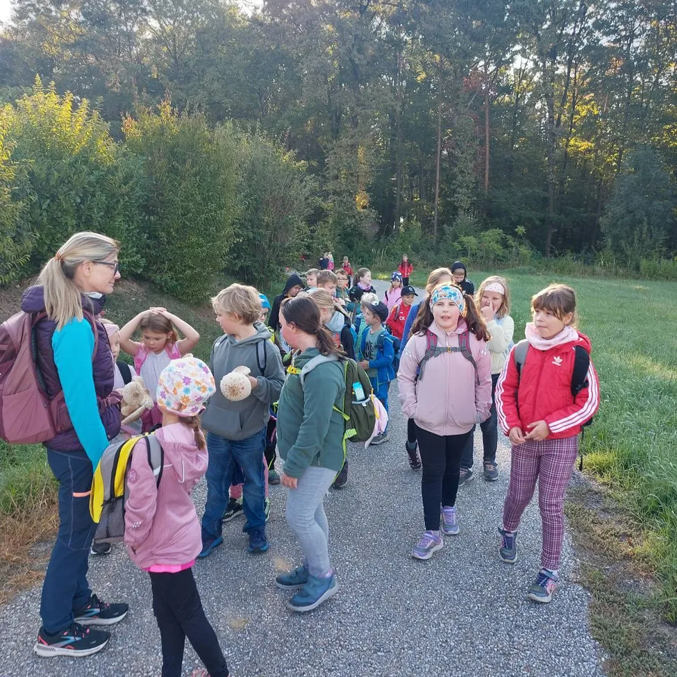 Eine Gruppe von Kindern, wahrscheinlich auf einer Schulfahrt, geht auf einem Kiesweg in einem Park. Sie werden von einer Frau begleitet, die wahrscheinlich ihre Lehrerin ist.