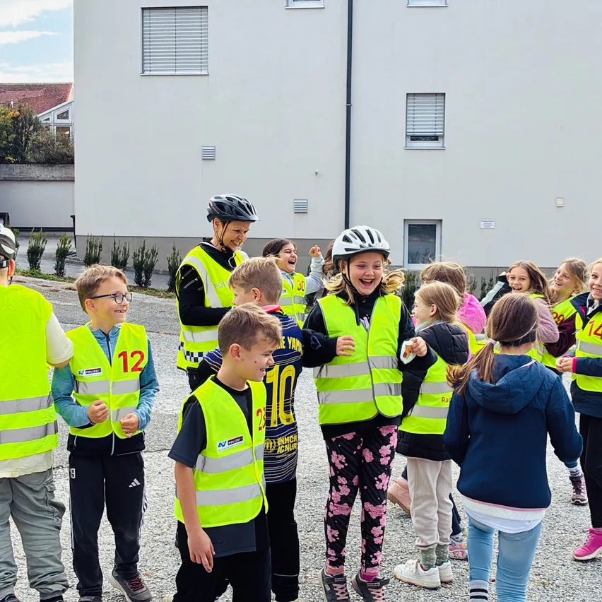 Eine Gruppe von Kindern und Erwachsenen versammelt sich auf einem Parkplatz. Sie tragen alle gelbe Sicherheitswesten.