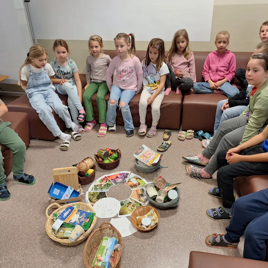 Eine Gruppe von Kindern sitzt in einem Kreis auf einer Couch mit Körben voller Essen vor ihnen.