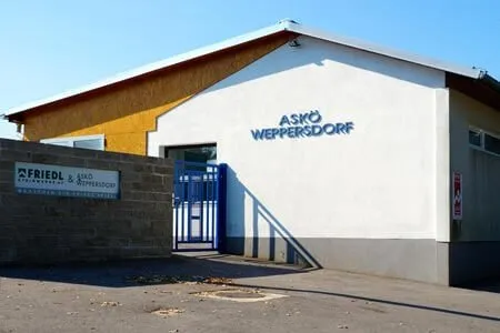 Das Äußere eines Gebäudes mit einem blauen Tor und einem Schild, das Askö Weppersdorf steht.